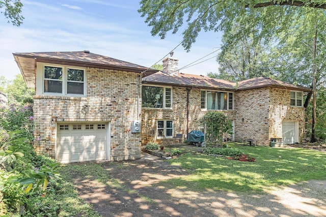view of front of house featuring a front yard, a chimney, brick siding, an attached garage, and driveway