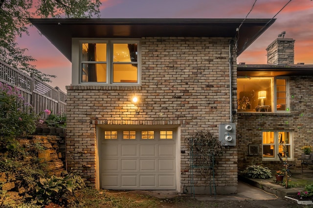 view of front of home featuring an attached garage, a chimney, and brick siding