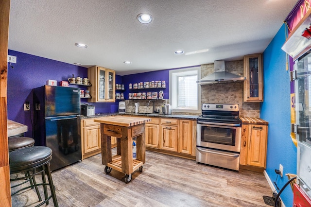 kitchen with a sink, wall chimney range hood, freestanding refrigerator, a textured ceiling, and stainless steel range with electric cooktop