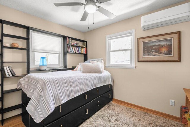 956 10th Ave SE, Forest Lake, MN 55025 - bedroom with a wall unit AC, baseboards, wood finished floors, and a ceiling fan