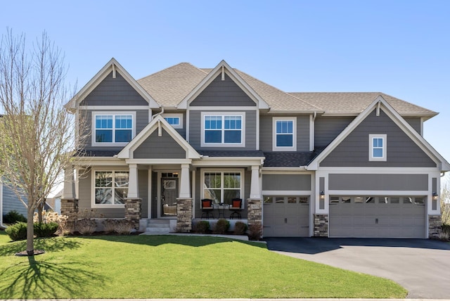 craftsman-style house featuring an attached garage, aphalt driveway, roof with shingles, and a front yard