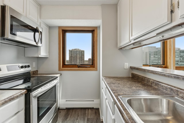 kitchen featuring dark wood finished floors, a sink, a baseboard radiator, white cabinets, and stainless steel appliances
