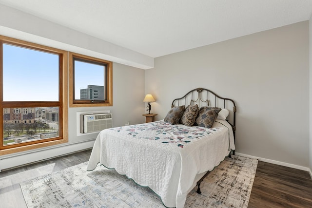 bedroom with baseboards, a baseboard heating unit, wood finished floors, and a wall mounted air conditioner