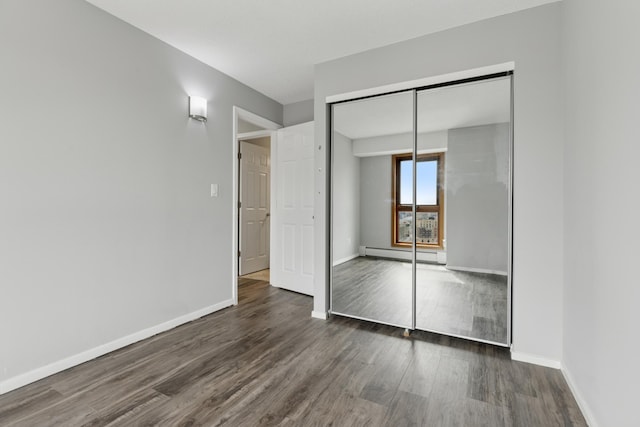 unfurnished bedroom featuring baseboards, a baseboard radiator, a closet, and dark wood-style flooring
