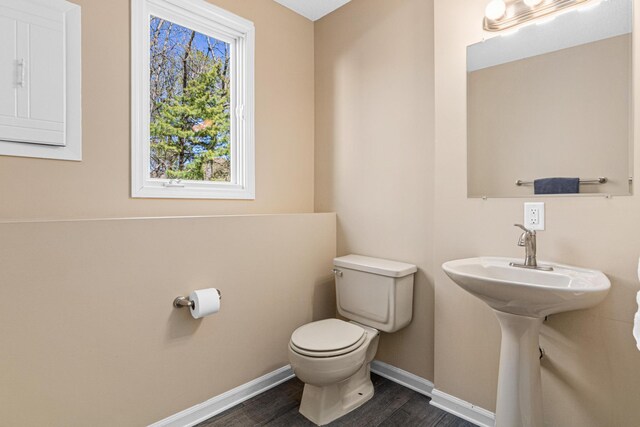half bathroom with a sink, baseboards, toilet, and wood finished floors
