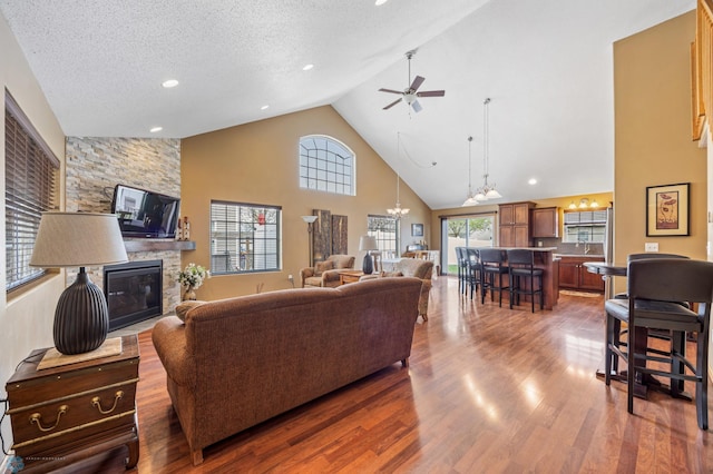living area with a fireplace, high vaulted ceiling, a chandelier, a ceiling fan, and wood finished floors