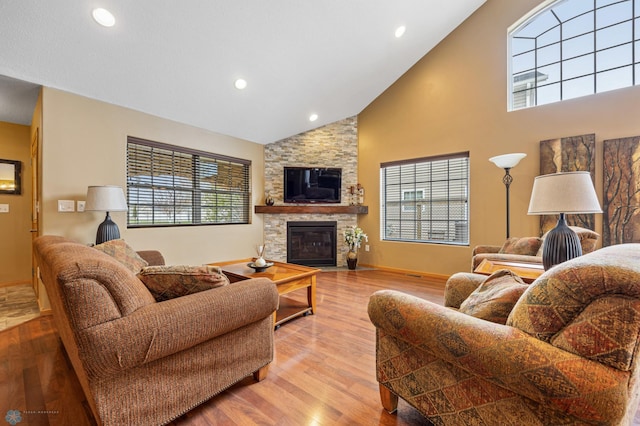 living area featuring high vaulted ceiling, wood finished floors, a stone fireplace, recessed lighting, and baseboards