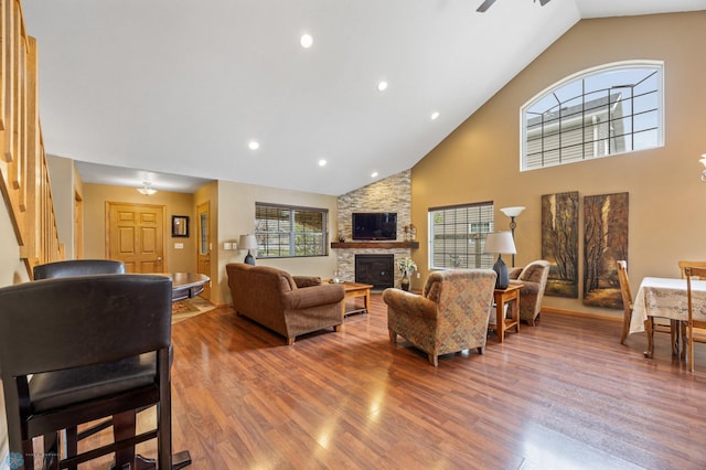 living room featuring wood finished floors, high vaulted ceiling, a fireplace, ceiling fan, and stairs
