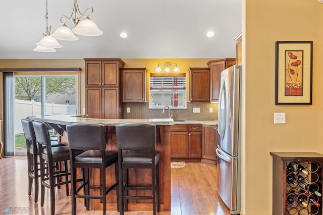 kitchen featuring freestanding refrigerator, a breakfast bar, brown cabinets, and recessed lighting