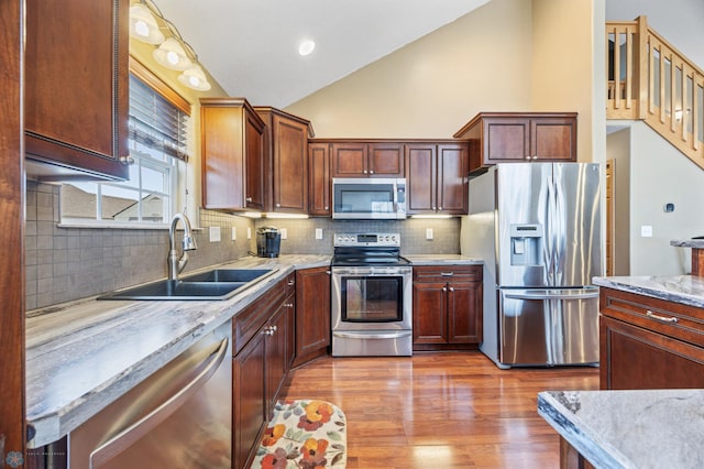 kitchen with stainless steel appliances, a sink, lofted ceiling, wood finished floors, and decorative backsplash