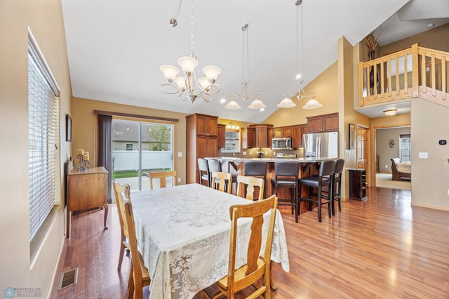 dining space featuring a chandelier, light wood-type flooring, high vaulted ceiling, and baseboards