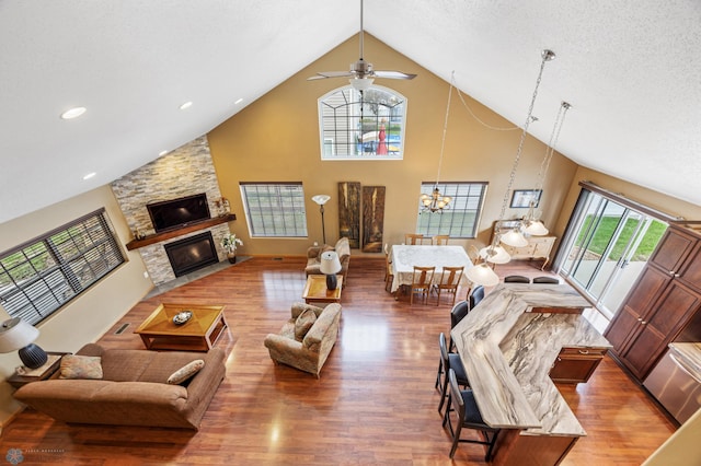 living area with wood finished floors, high vaulted ceiling, a stone fireplace, ceiling fan, and recessed lighting