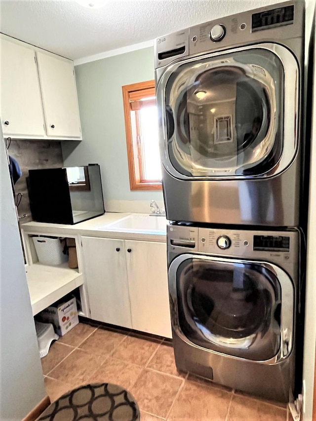 clothes washing area featuring stacked washer / drying machine, cabinet space, a textured ceiling, and light tile patterned floors