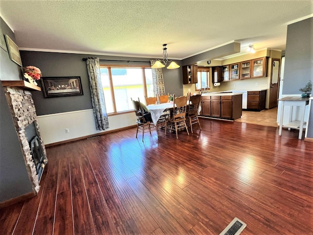 dining area with wood finished floors, a textured ceiling, ornamental molding, wainscoting, and a fireplace