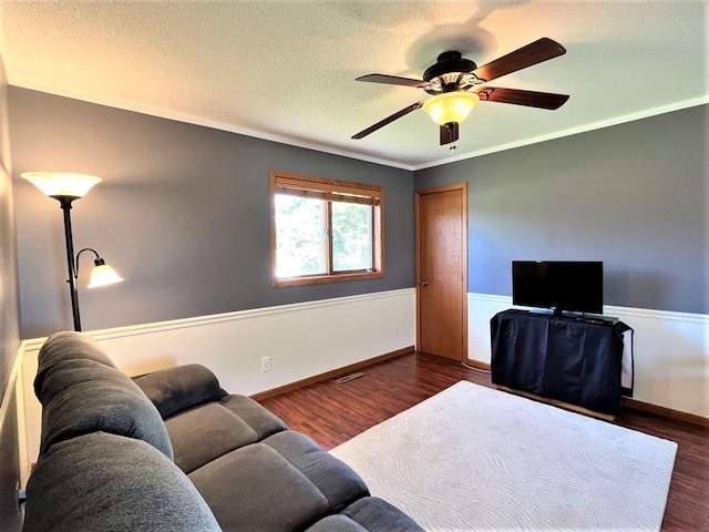 living area featuring ceiling fan, dark wood-style flooring, a textured ceiling, a wainscoted wall, and baseboards