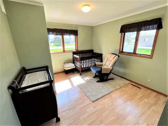 bedroom with ornamental molding, wood finished floors, baseboards, a crib, and a textured ceiling