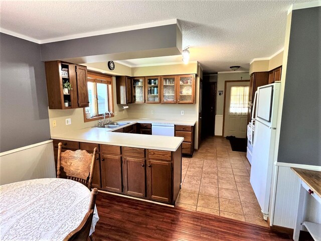 kitchen with a sink, white appliances, a peninsula, light countertops, and glass insert cabinets
