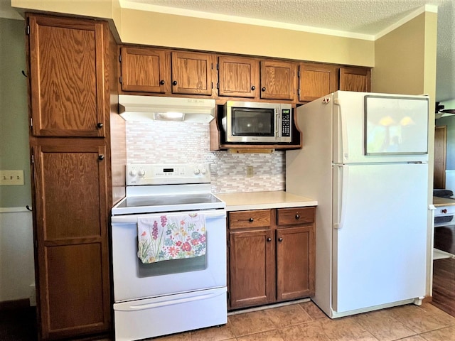 kitchen with white appliances, under cabinet range hood, light countertops, brown cabinetry, and backsplash