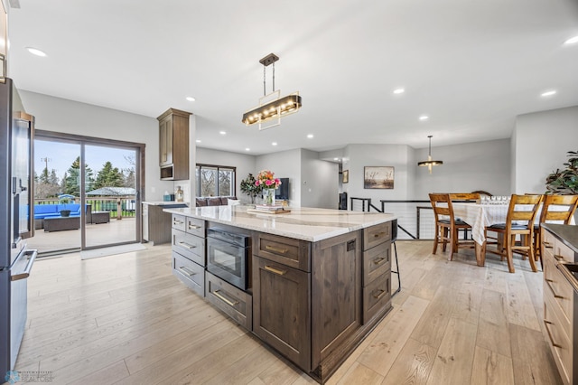 134 Newport Pkwy N, Kindred, ND 58051 - kitchen with light stone countertops, pendant lighting, dark brown cabinetry, black microwave, and light wood-type flooring