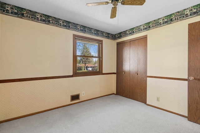unfurnished bedroom with wallpapered walls, carpet, a closet, baseboards, and ceiling fan