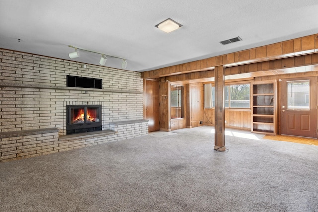 unfurnished living room with wooden walls, carpet floors, a fireplace, a textured ceiling, and rail lighting