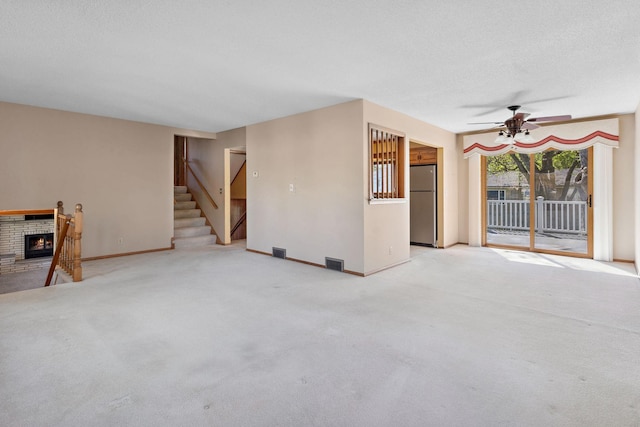empty room featuring a ceiling fan, a fireplace, light carpet, stairs, and baseboards