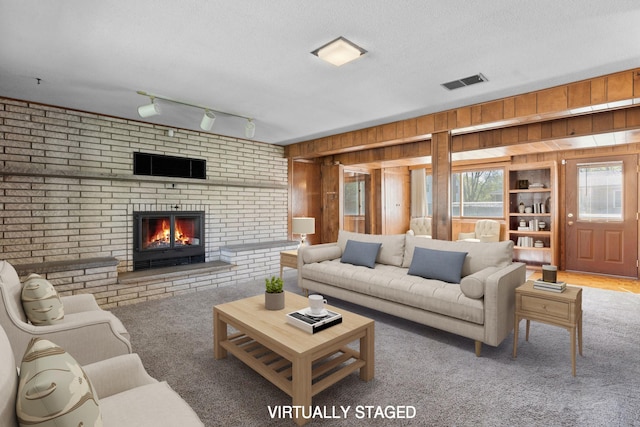 living area featuring wood walls, a fireplace, carpet floors, and a textured ceiling
