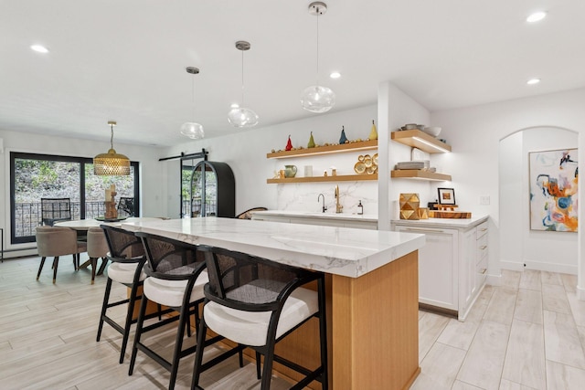 215 Barry Ave S Unit 116And 114, Wayzata, MN 55391 - kitchen with open shelves, a barn door, arched walkways, white cabinets, and a center island