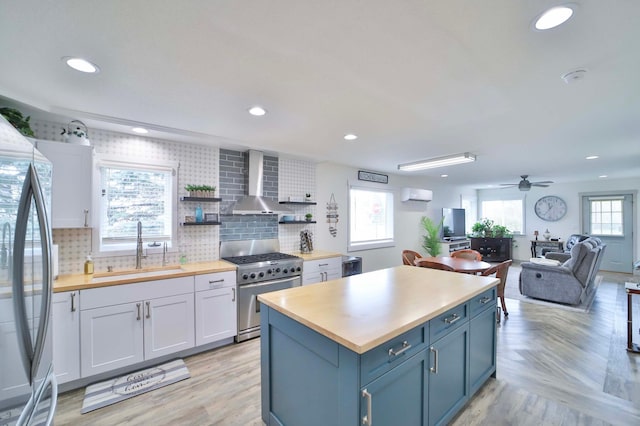 kitchen with appliances with stainless steel finishes, a sink, wooden counters, wall chimney exhaust hood, and decorative backsplash