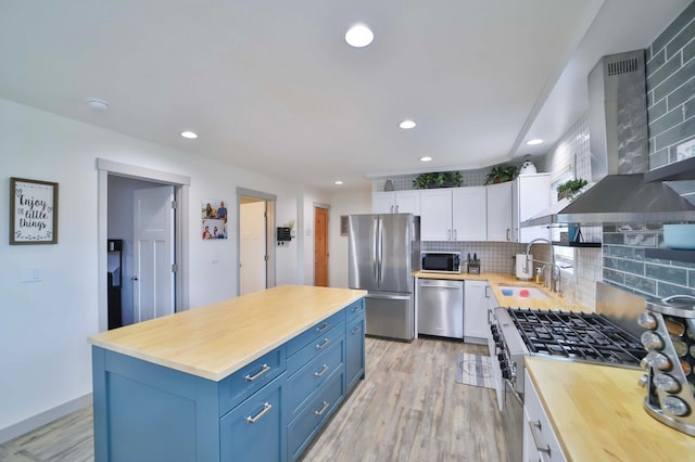 kitchen with wall chimney exhaust hood, white cabinets, a sink, wood counters, and appliances with stainless steel finishes