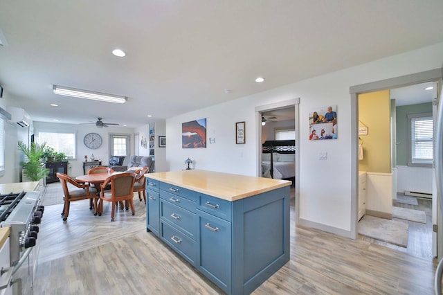 kitchen featuring a ceiling fan, blue cabinets, gas stove, open floor plan, and light wood-style floors