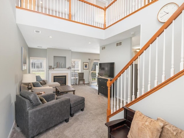 living room with visible vents, carpet flooring, stairs, and a towering ceiling