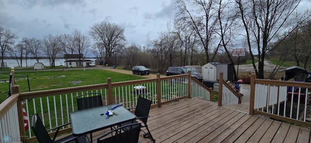 wooden terrace with an outdoor structure, a storage unit, a lawn, a water view, and outdoor dining space