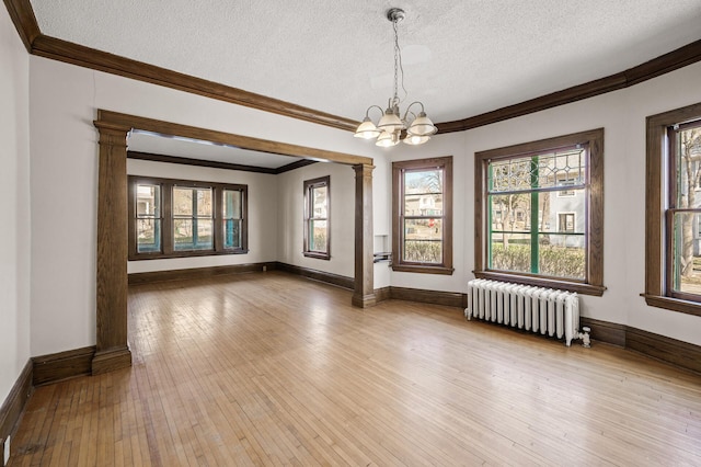 unfurnished room with ornamental molding, decorative columns, radiator heating unit, a textured ceiling, and hardwood / wood-style flooring