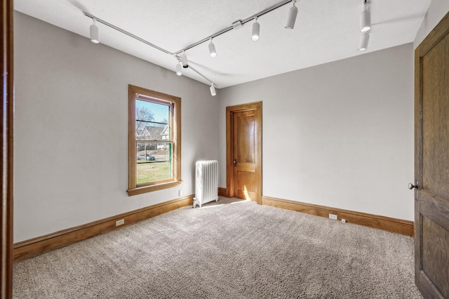 carpeted empty room with radiator heating unit, baseboards, and rail lighting