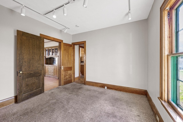 empty room featuring track lighting, baseboards, and carpet floors