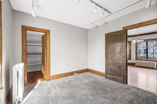 unfurnished room with carpet flooring, an inviting chandelier, rail lighting, radiator, and baseboards