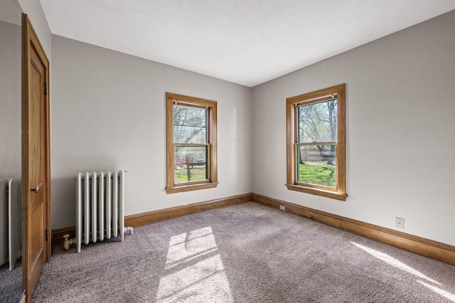 carpeted spare room with a healthy amount of sunlight, radiator, and baseboards