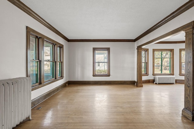 unfurnished room featuring crown molding, ornate columns, radiator, and hardwood / wood-style floors