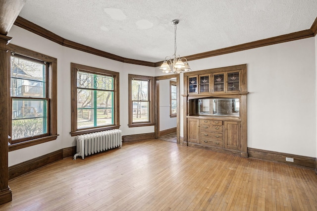 unfurnished dining area featuring a textured ceiling, crown molding, baseboards, a notable chandelier, and radiator heating unit