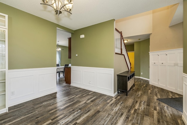 empty room featuring stairs, dark wood-style flooring, wainscoting, and a chandelier