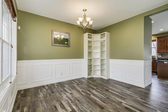 unfurnished dining area featuring visible vents, a wainscoted wall, a notable chandelier, a decorative wall, and dark wood-type flooring