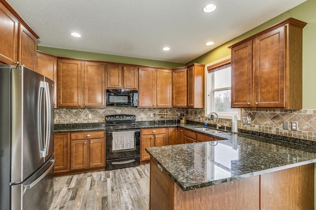 kitchen with a sink, black appliances, dark stone countertops, light wood finished floors, and a peninsula
