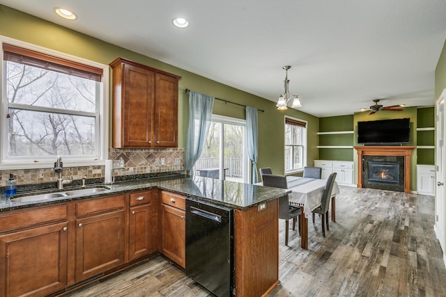 kitchen featuring a glass covered fireplace, open floor plan, a sink, light wood-style flooring, and dishwasher