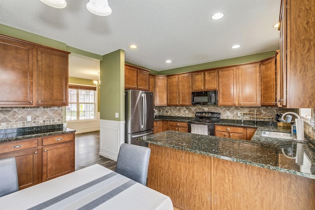 kitchen featuring a sink, dark stone counters, black appliances, and dark wood-type flooring