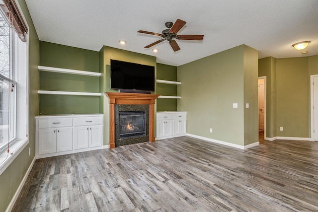 unfurnished living room with ceiling fan, wood finished floors, a wealth of natural light, and a premium fireplace