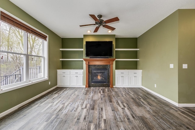 unfurnished living room with baseboards, a glass covered fireplace, wood finished floors, and ceiling fan
