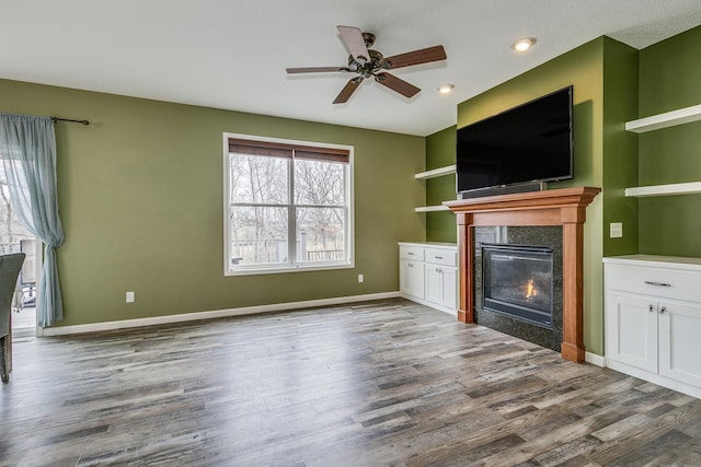 unfurnished living room with baseboards, a glass covered fireplace, wood finished floors, and ceiling fan