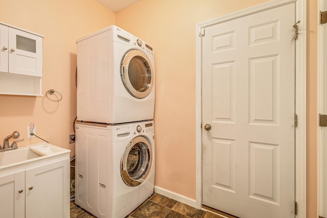 laundry area with baseboards, a sink, cabinet space, and stacked washing maching and dryer