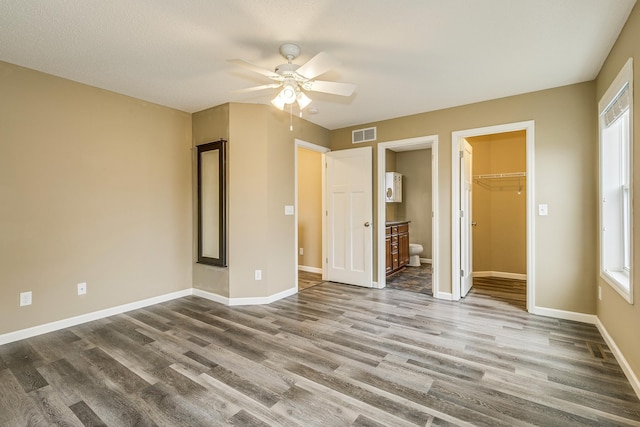 unfurnished bedroom with a walk in closet, visible vents, wood finished floors, baseboards, and connected bathroom